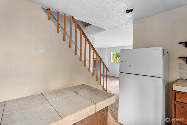 kitchen featuring a textured ceiling, tile counters, white fridge, and light tile patterned floors