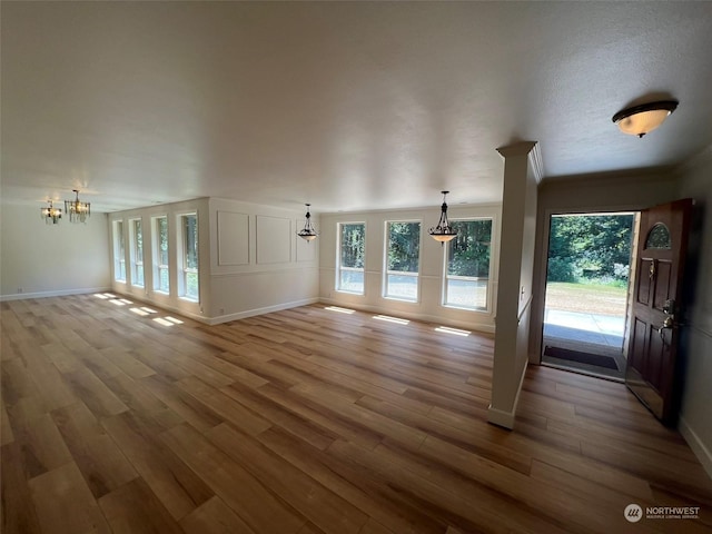 unfurnished living room with a notable chandelier, light hardwood / wood-style floors, and crown molding