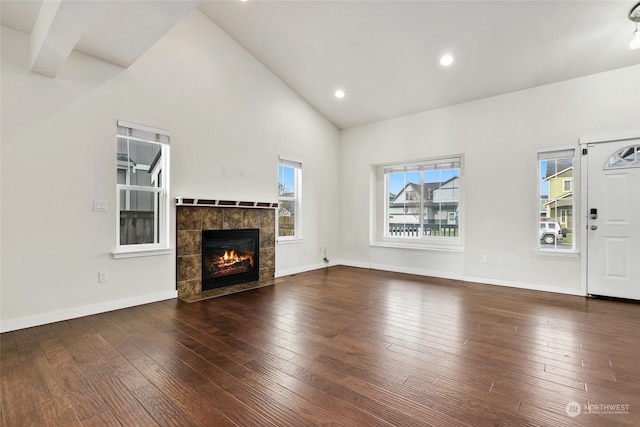 unfurnished living room featuring dark hardwood / wood-style flooring, high vaulted ceiling, and a tiled fireplace