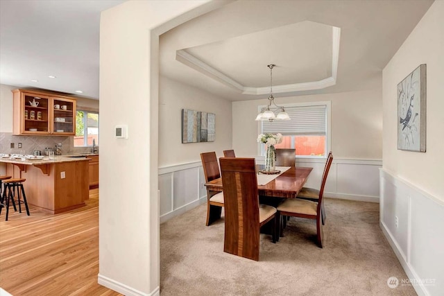 dining room featuring light carpet, a raised ceiling, a notable chandelier, and sink