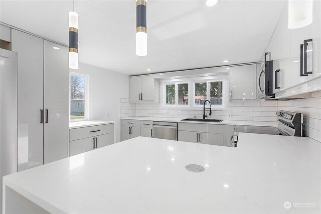 kitchen featuring pendant lighting, sink, decorative backsplash, a wealth of natural light, and stainless steel appliances