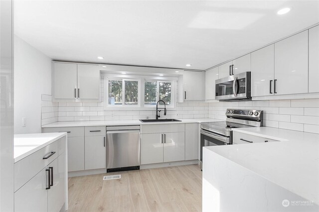 kitchen with white cabinets, appliances with stainless steel finishes, light wood-type flooring, and sink