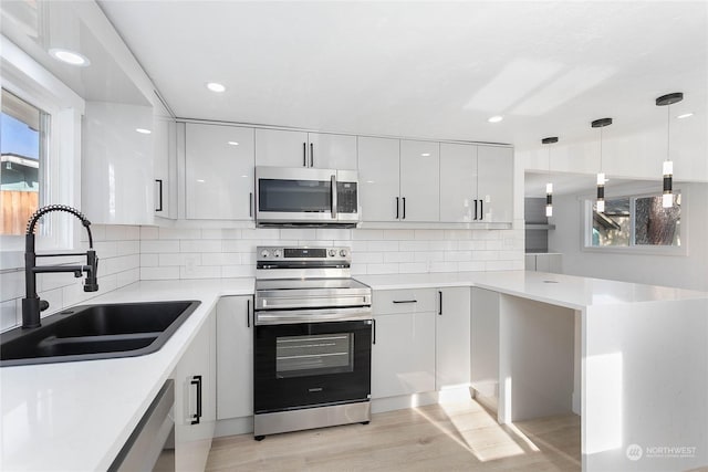 kitchen featuring kitchen peninsula, stainless steel appliances, sink, white cabinetry, and hanging light fixtures