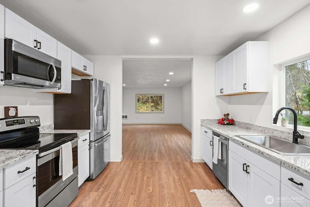 kitchen with appliances with stainless steel finishes, light wood-type flooring, white cabinetry, and a sink