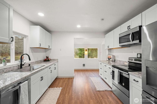 kitchen featuring light wood finished floors, recessed lighting, appliances with stainless steel finishes, white cabinetry, and a sink