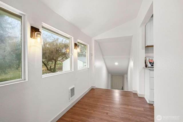 hall featuring baseboards, visible vents, vaulted ceiling, and wood finished floors