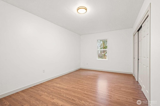 unfurnished bedroom with light wood-type flooring, a closet, and baseboards