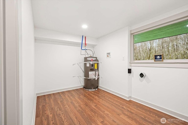 laundry area with wood finished floors, secured water heater, baseboards, and laundry area