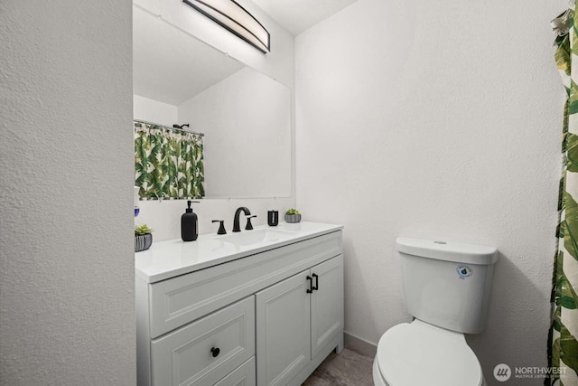 full bath featuring a textured wall, vanity, and toilet