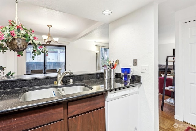 kitchen featuring white dishwasher, sink, an inviting chandelier, light hardwood / wood-style flooring, and dark stone countertops