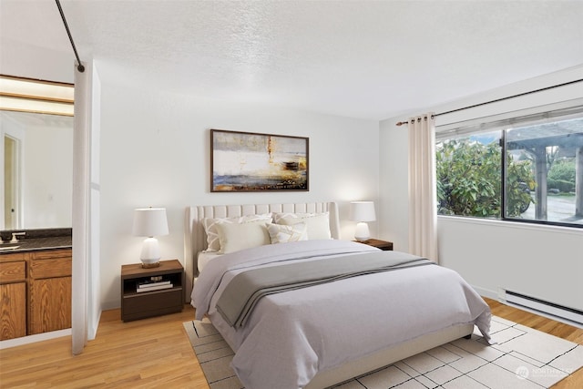 bedroom featuring a baseboard heating unit, a textured ceiling, and light hardwood / wood-style flooring