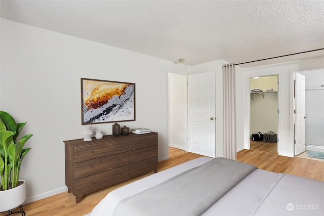 bedroom with a textured ceiling, light hardwood / wood-style flooring, a spacious closet, and a closet