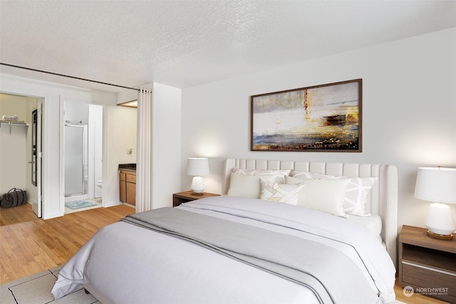 bedroom featuring ensuite bath, a textured ceiling, a spacious closet, light hardwood / wood-style floors, and a closet