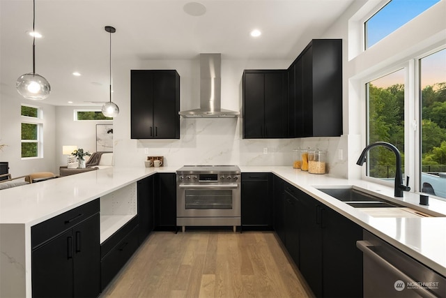 kitchen with kitchen peninsula, decorative light fixtures, stainless steel appliances, and wall chimney range hood