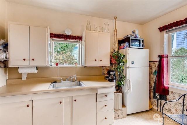 kitchen featuring white fridge, white cabinetry, a healthy amount of sunlight, and sink