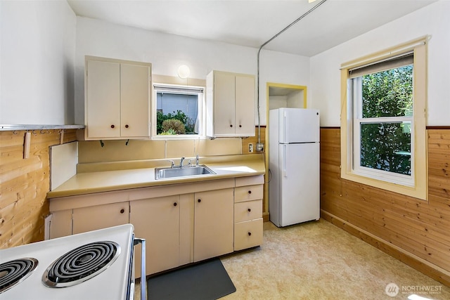 kitchen featuring a wainscoted wall, light countertops, a sink, wooden walls, and white appliances