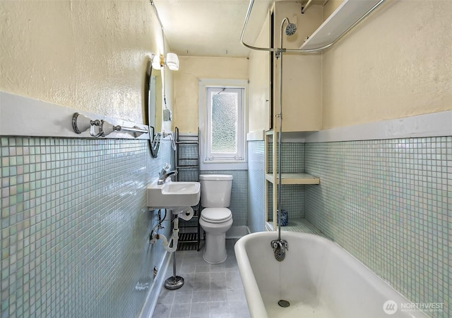 full bathroom with a bathing tub, toilet, a sink, tile walls, and tile patterned floors