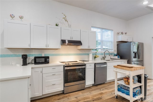 kitchen with decorative backsplash, stainless steel appliances, sink, white cabinets, and light hardwood / wood-style floors