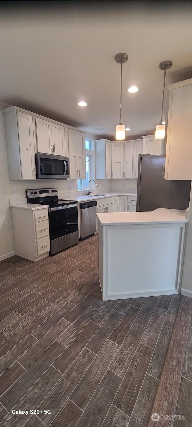 kitchen with appliances with stainless steel finishes, pendant lighting, sink, white cabinets, and kitchen peninsula