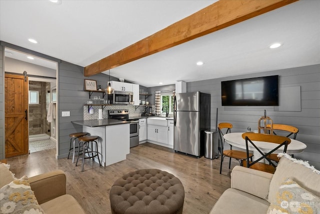 kitchen featuring hanging light fixtures, a barn door, white cabinetry, appliances with stainless steel finishes, and vaulted ceiling with beams