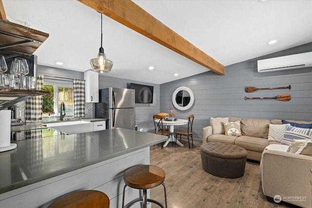 kitchen with a wall unit AC, light hardwood / wood-style floors, lofted ceiling with beams, stainless steel fridge, and decorative light fixtures