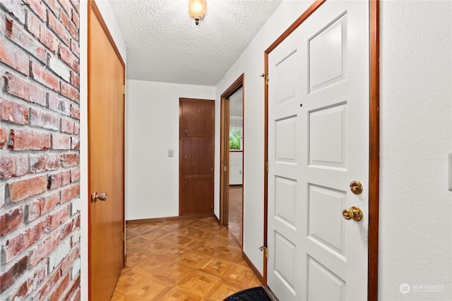 hall with a textured ceiling, brick wall, and light parquet floors