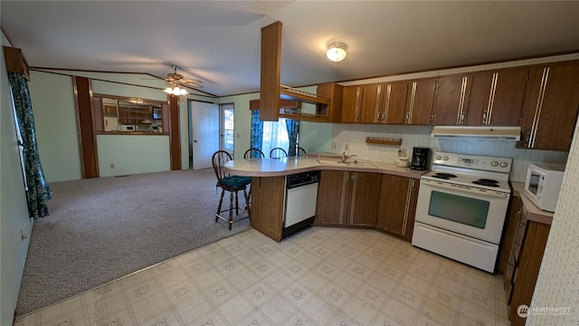 kitchen featuring white appliances, light carpet, sink, kitchen peninsula, and a breakfast bar area