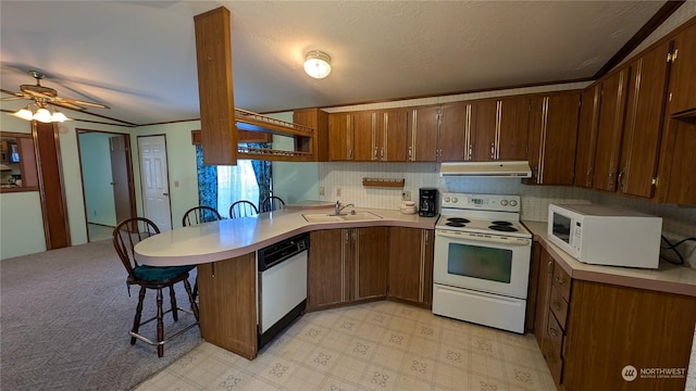 kitchen with white appliances, sink, kitchen peninsula, vaulted ceiling, and a breakfast bar