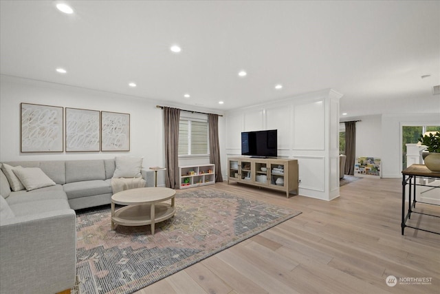 living room featuring light wood-type flooring, a wealth of natural light, and ornamental molding