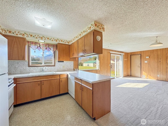 kitchen with wooden walls, light countertops, a peninsula, white appliances, and a sink