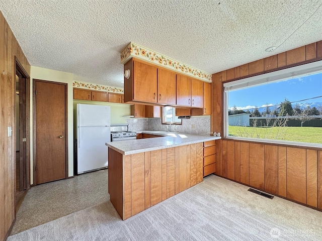 kitchen featuring white appliances, brown cabinetry, visible vents, a peninsula, and light countertops