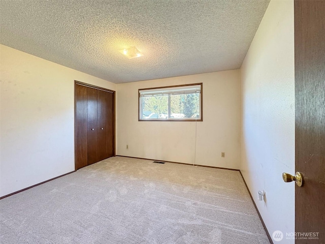 unfurnished bedroom with visible vents, light colored carpet, a closet, and a textured ceiling