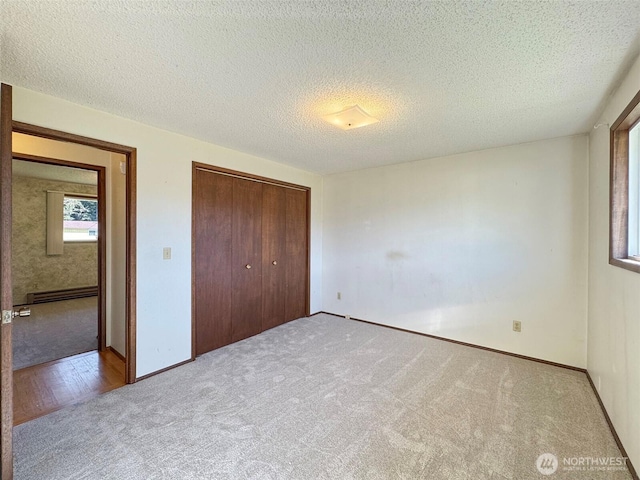 unfurnished bedroom with a textured ceiling, a closet, carpet floors, a baseboard radiator, and baseboards