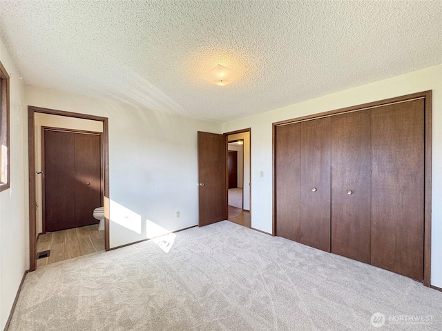 unfurnished bedroom with visible vents, ensuite bath, carpet floors, a closet, and a textured ceiling