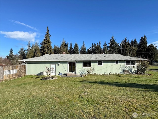 rear view of property featuring a lawn, central AC, and fence