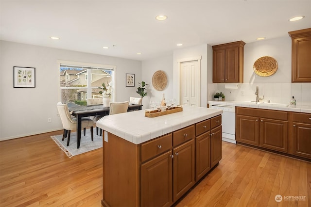 kitchen with sink, dishwasher, a center island, light hardwood / wood-style floors, and tile counters