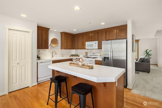 kitchen with tile countertops, sink, white appliances, and light hardwood / wood-style flooring