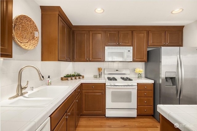 kitchen featuring tile countertops, white appliances, sink, and light hardwood / wood-style flooring