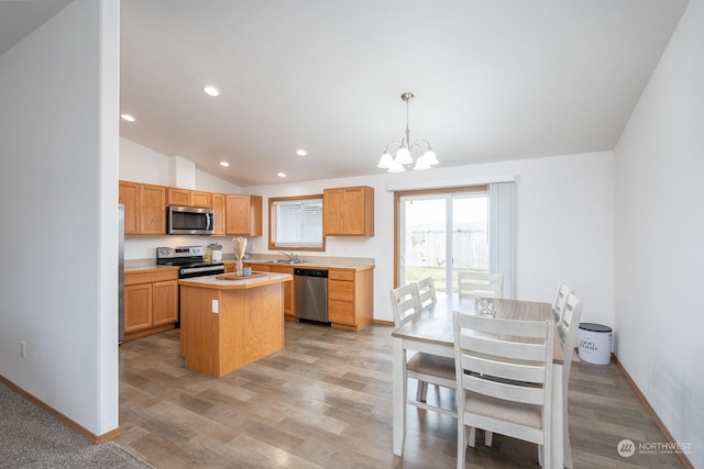 kitchen featuring vaulted ceiling, appliances with stainless steel finishes, hanging light fixtures, a center island, and sink