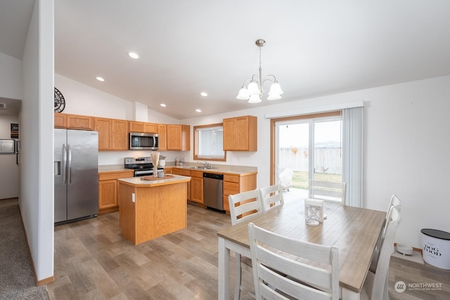 kitchen with vaulted ceiling, appliances with stainless steel finishes, a center island, a notable chandelier, and decorative light fixtures