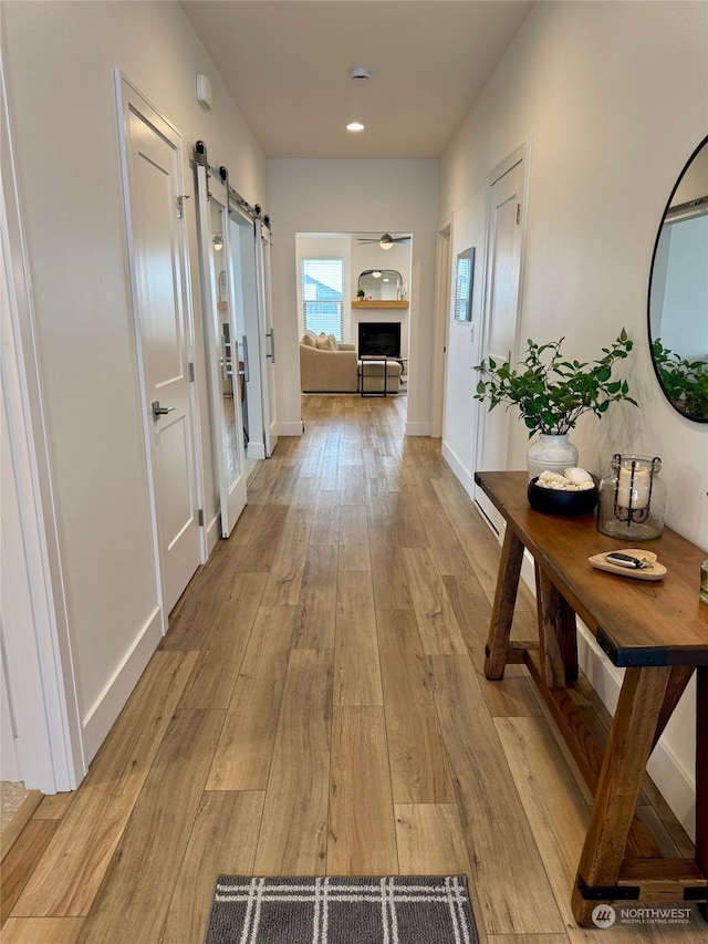 hallway featuring baseboards, light wood-type flooring, and a barn door