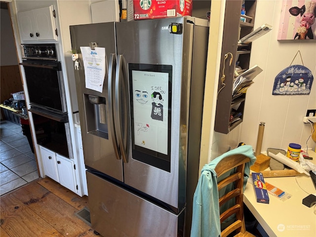 kitchen featuring white cabinetry, stainless steel fridge, black double oven, and tile patterned floors