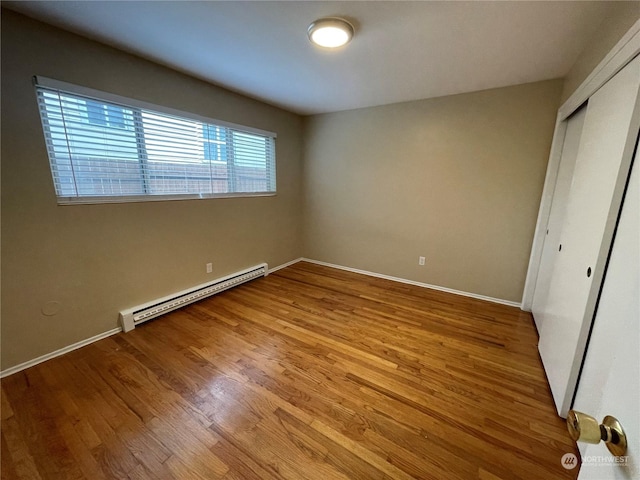 unfurnished bedroom featuring hardwood / wood-style flooring, a baseboard radiator, and a closet