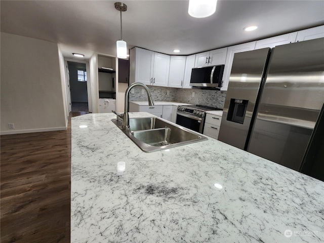 kitchen with pendant lighting, decorative backsplash, white cabinets, stainless steel appliances, and a sink