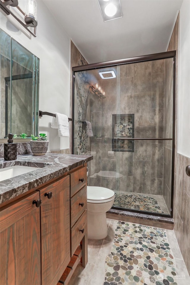 bathroom featuring tile patterned floors, toilet, vanity, a shower with shower door, and tile walls