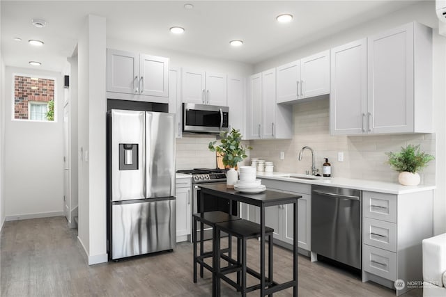 kitchen featuring wood finished floors, a sink, white cabinetry, light countertops, and appliances with stainless steel finishes