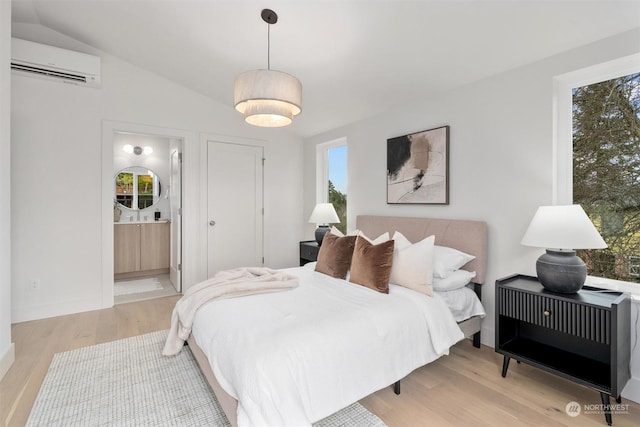 bedroom with light hardwood / wood-style floors, an AC wall unit, connected bathroom, and multiple windows