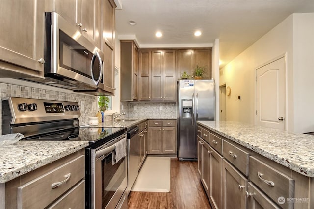 kitchen with a center island, light stone counters, dark hardwood / wood-style flooring, backsplash, and appliances with stainless steel finishes