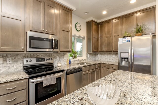 kitchen featuring decorative backsplash, light stone countertops, sink, and stainless steel appliances