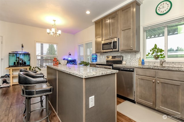 kitchen with sink, dark wood-type flooring, stainless steel appliances, a chandelier, and a kitchen island